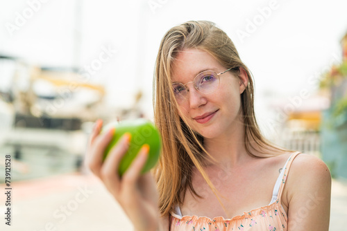 Young French girl with glasses at outdoors holding an apple with happy expression
