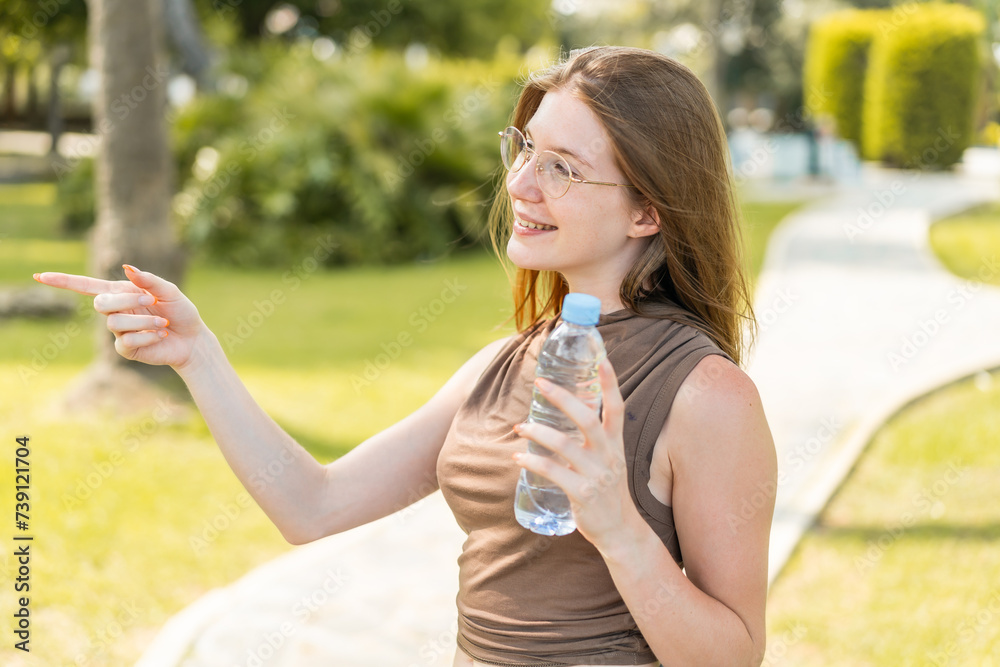 French girl with glasses holding a bottle of water at outdoors pointing to the side to present a product French girl with glasses holding a bottle of water at outdoors pointing to the side to present a product