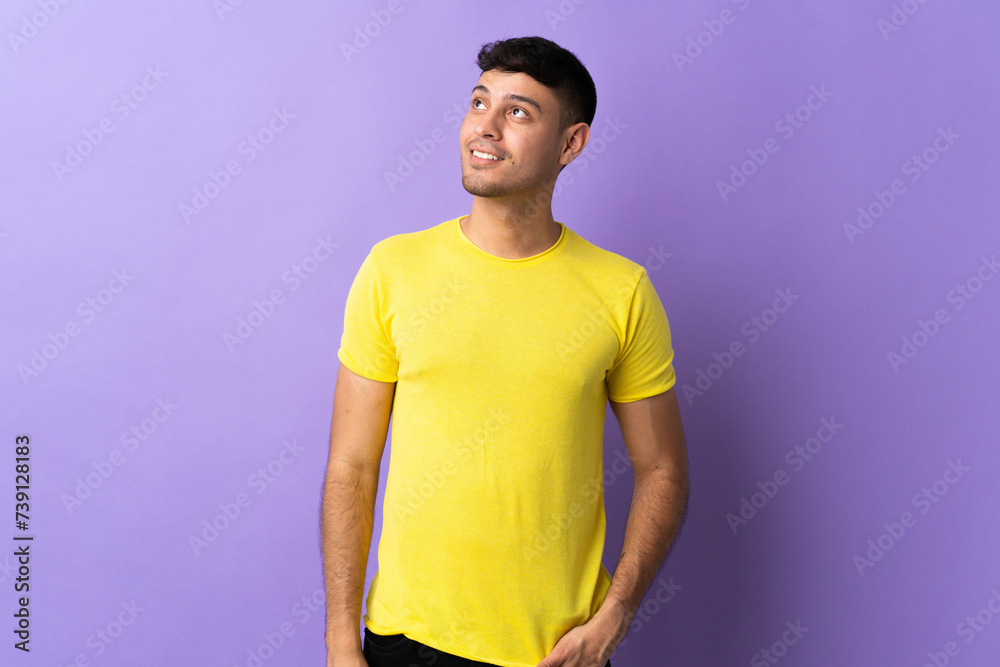Young Colombian man isolated on purple background thinking an idea while looking up