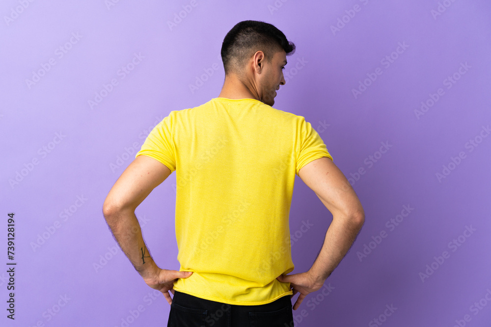Young Colombian man isolated on purple background in back position and looking side