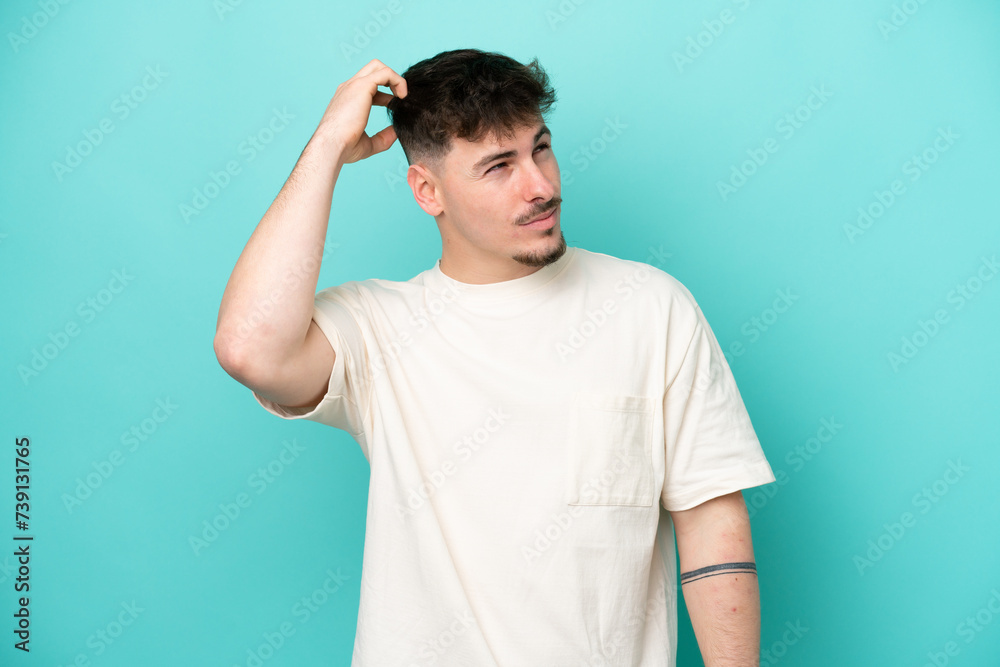 Young caucasian handsome man isolated on blue background having doubts while scratching head Young caucasian handsome man isolated on blue background having doubts while scratching head