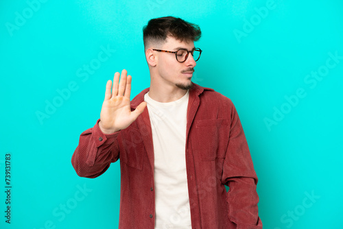 Young caucasian handsome man isolated on blue background making stop gesture and disappointed