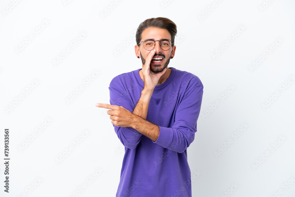 Young caucasian man isolated on white background pointing to the side to present a product and whispering something Young caucasian man isolated on white background pointing to the side to present a product and whispering something