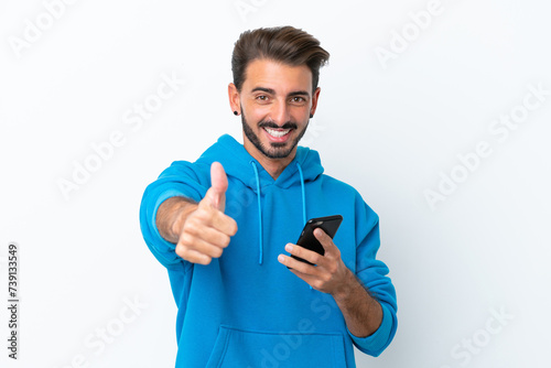 Young caucasian man isolated on white background using mobile phone while doing thumbs up