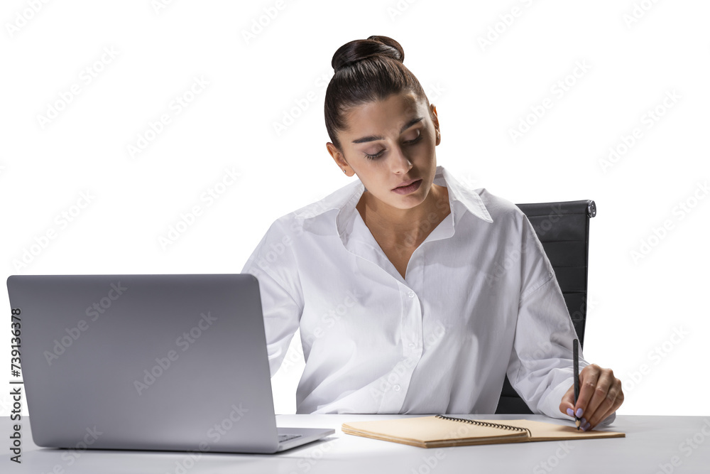 Focused businesswoman at desk writing in notebook with laptop, office work concept Focused businesswoman at desk writing in notebook with laptop, office work concept