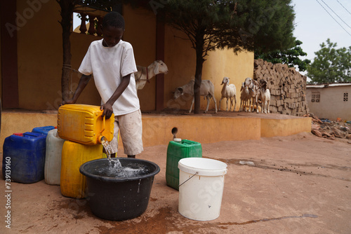 Young African village boy filling water containers in his backyard ; concept of rural lifestyle in developing countries