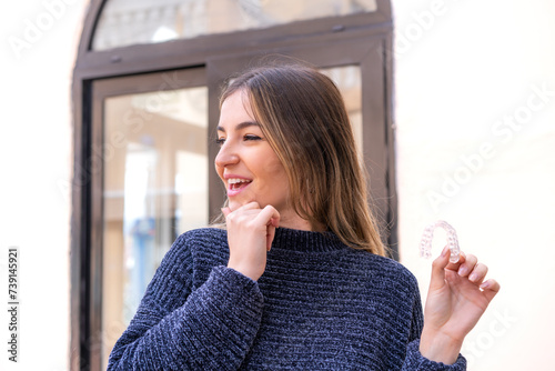 Young pretty Romanian woman holding invisible braces at outdoors thinking an idea and looking side
