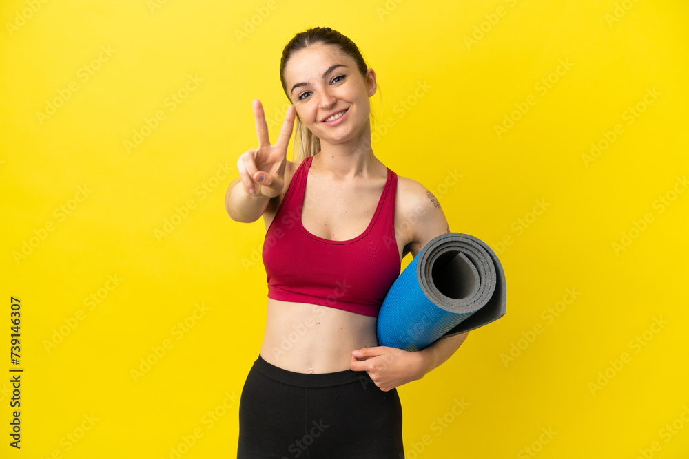 Young sport woman going to yoga classes while holding a mat smiling and showing victory sign Young sport woman going to yoga classes while holding a mat smiling and showing victory sign