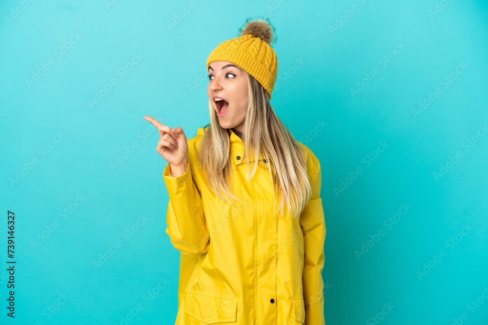 Young woman wearing a rainproof coat over isolated blue background intending to realizes the solution while lifting a finger up Young woman wearing a rainproof coat over isolated blue background intending to realizes the solution while lifting a finger up