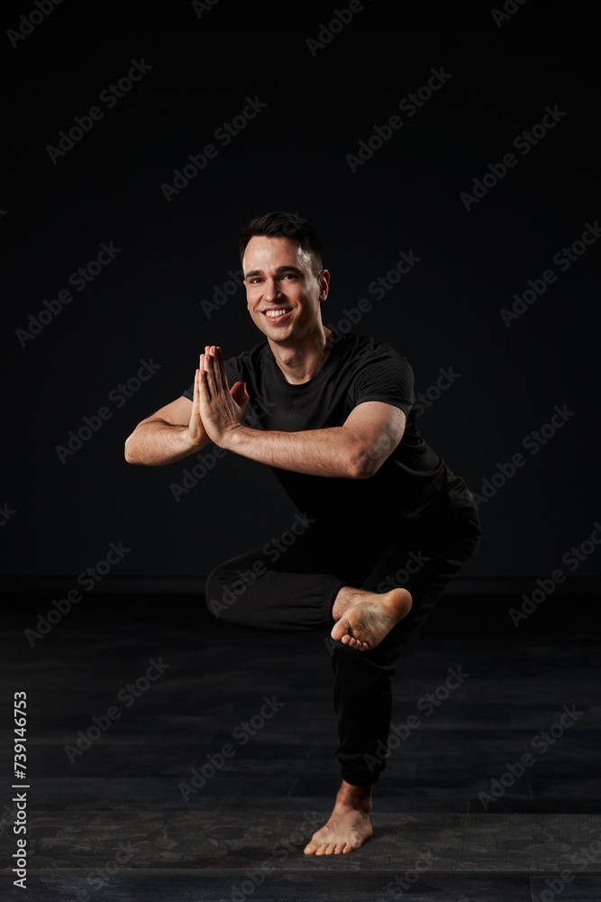 The handsome young man, donned in black, performs a mesmerizing ballet of yoga on his mat, each pose a brushstroke of poise and strength.