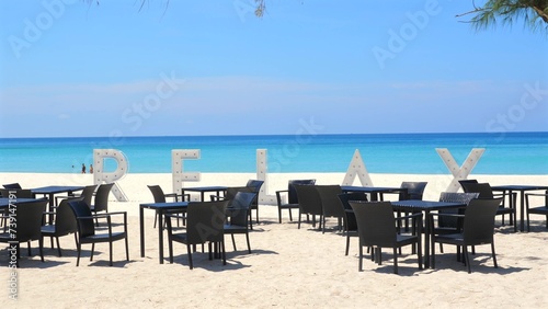 Tropical beach restaurant with RELAX sign set up on white sand facing serene ocean. Idyllic vacation spot for dining and unwinding. Leisure travel and tourism.