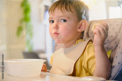Baby boy eats cookies in a cafe. Child in a restaurant sitting at a table on a high chair. Kid aged two years