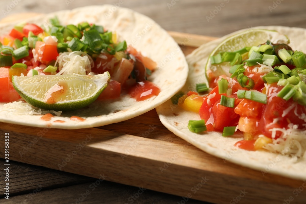 Delicious tacos with vegetables, green onion, lime and ketchup on wooden table, closeup