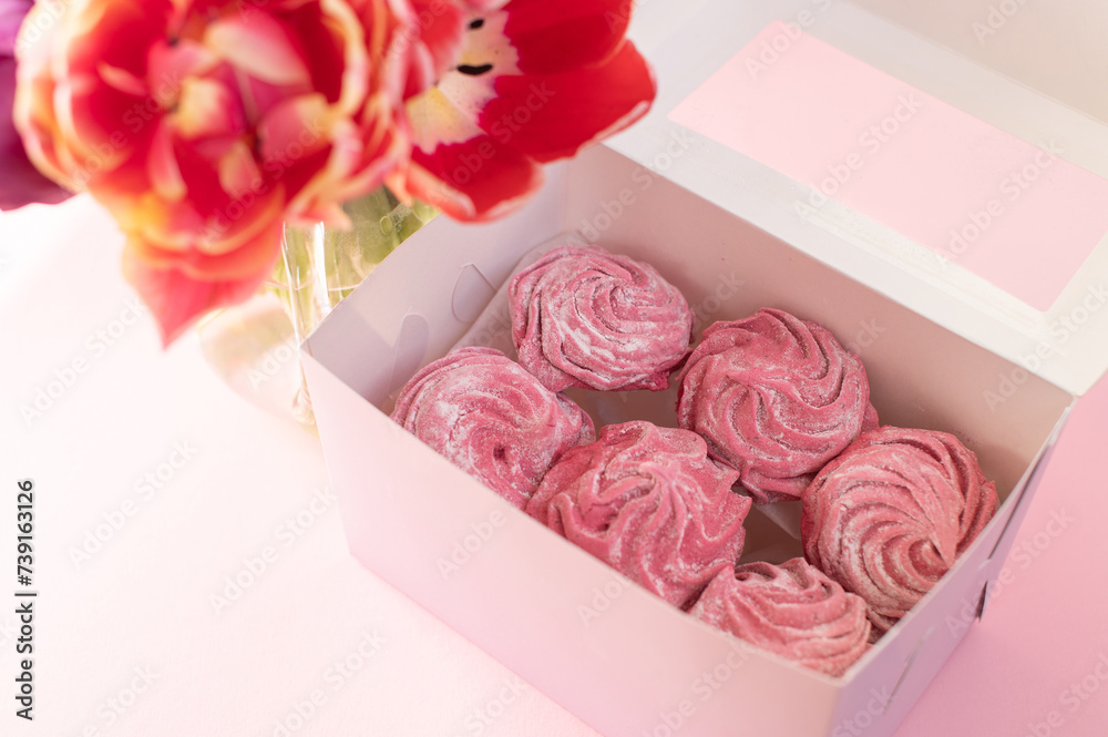 Pink marshmallow lies in a gift box near a vase with tulips on a pink background Pink marshmallow lies in a gift box near a vase with tulips on a pink background