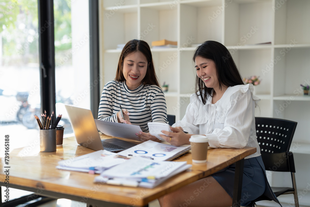 Two smiling female colleagues collaborate on paperwork with a laptop, notebooks in a contemporary office space. Two smiling female colleagues collaborate on paperwork with a laptop, notebooks in a contemporary office space.