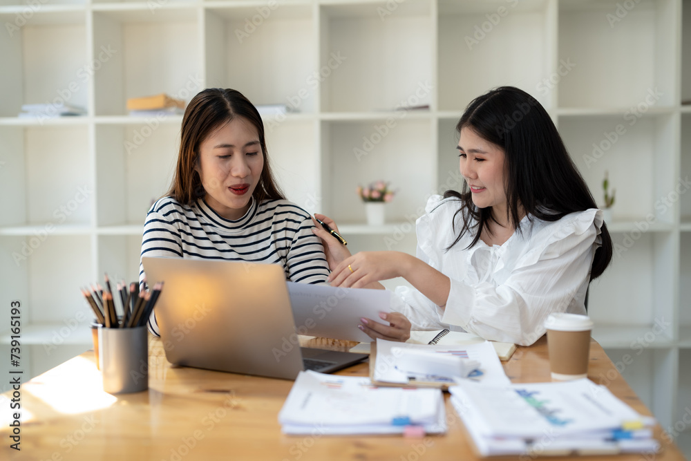 Two smiling female colleagues collaborate on paperwork with a laptop, notebooks in a contemporary office space. Two smiling female colleagues collaborate on paperwork with a laptop, notebooks in a contemporary office space.