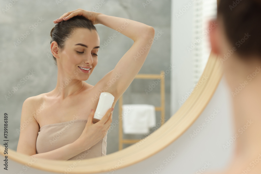 Beautiful woman applying deodorant near mirror in bathroom Beautiful woman applying deodorant near mirror in bathroom