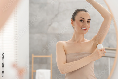 Beautiful woman applying deodorant near mirror in bathroom