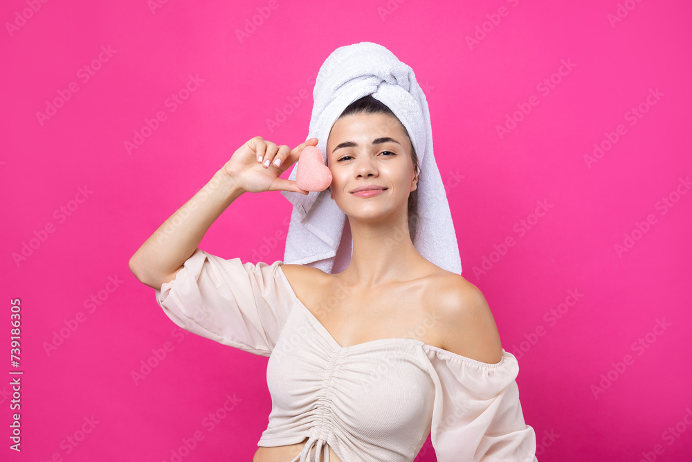 Beautiful cheerful attractive girl with a towel on her head, holds a sponge in the form of a pink heart.