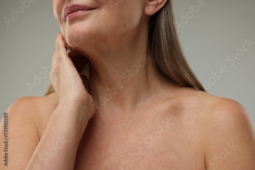 Mature woman touching her neck on grey background, closeup photo