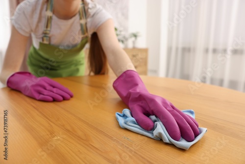 Woman with microfiber cloth cleaning wooden table in room, closeup