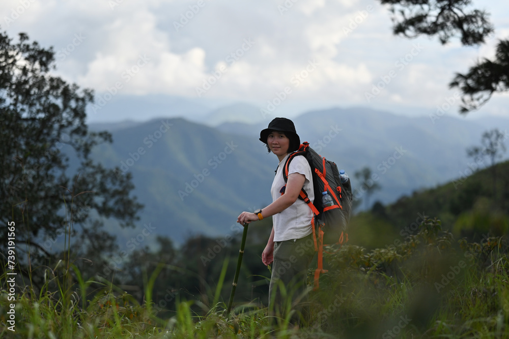 An Asian woman with a backpack and trekking pole standing and enjoying the fresh air while hiking on the mountain, Solo travel concept