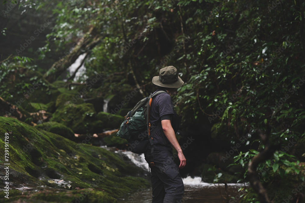 Rear view of Adventure man traveler exploring a waterfall in the forest, Traveling along mountains and rainforest, Solo travel concept