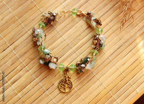Delicate vintage bracelet made of a mix of natural stones jasper, jade with a golden tree of life pendant on a bamboo background.