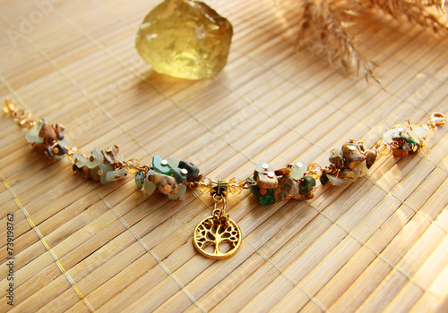Delicate vintage bracelet made of a mix of natural stones jasper, jade with a golden tree of life pendant on a bamboo background.