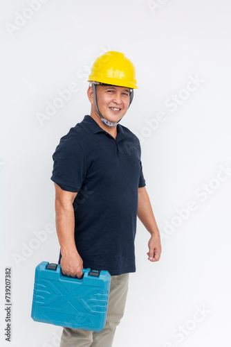 A middle-aged Asian man in a black shirt, wearing a hardhat, holding a toolbox, smiling confidently isolated on white.