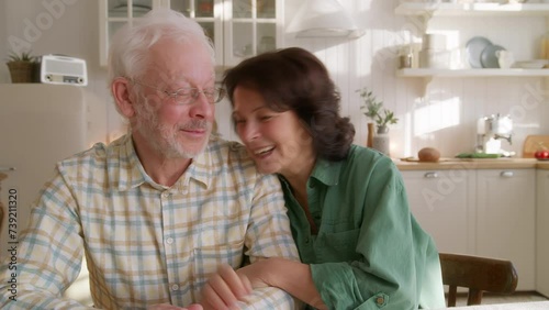 warmth portrait of longlife loved elderly couple. sitting at table at home, hugging and holding each other hands. looks happy and tender photo