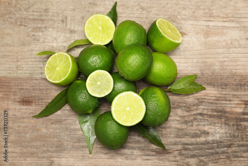 Pile of fresh limes and green leaves on wooden table, flat lay