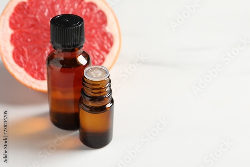 Grapefruit essential oil in bottles and fruit on white table, closeup. Space for text