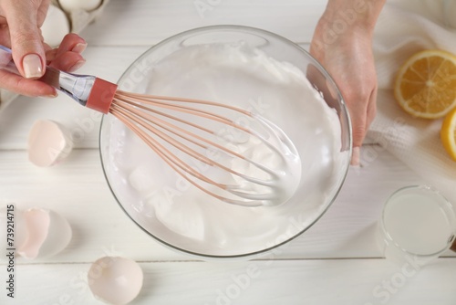 Woman making whipped cream with whisk at white wooden table, above view photo