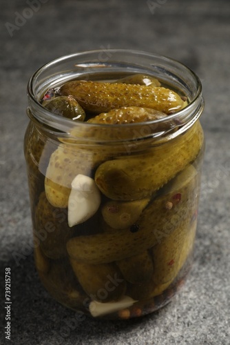 Tasty pickled cucumbers in glass jar on grey table, closeup