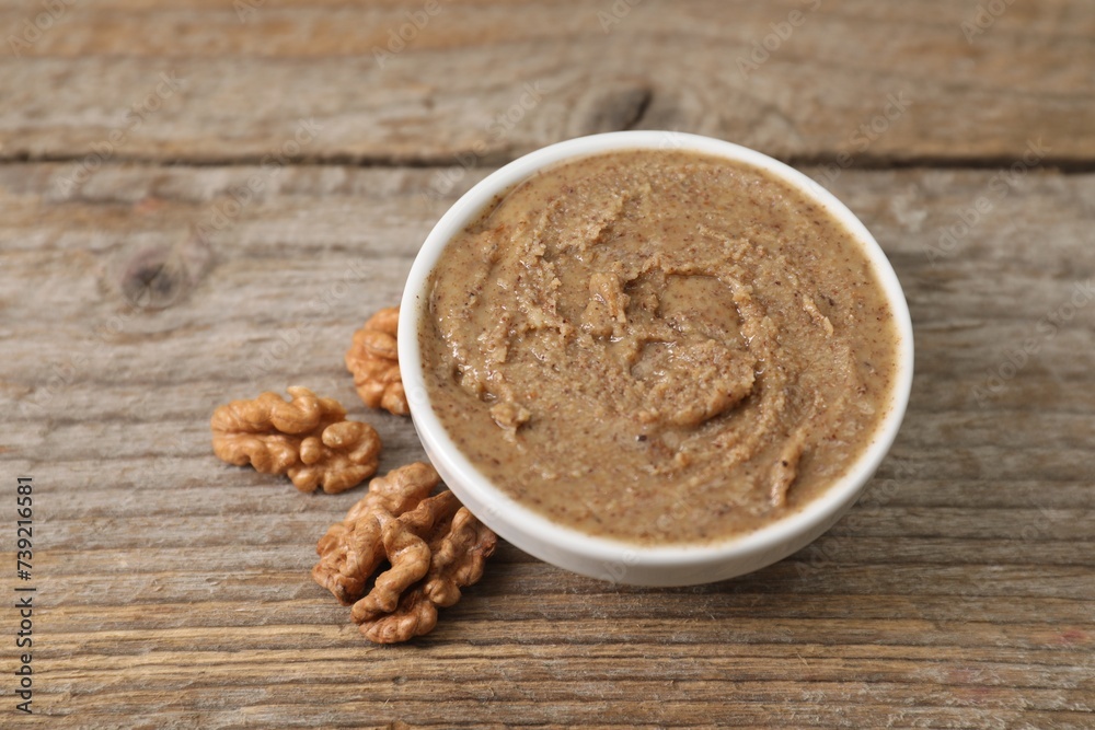 Delicious nut butter in bowl and walnuts on wooden table, closeup Delicious nut butter in bowl and walnuts on wooden table, closeup