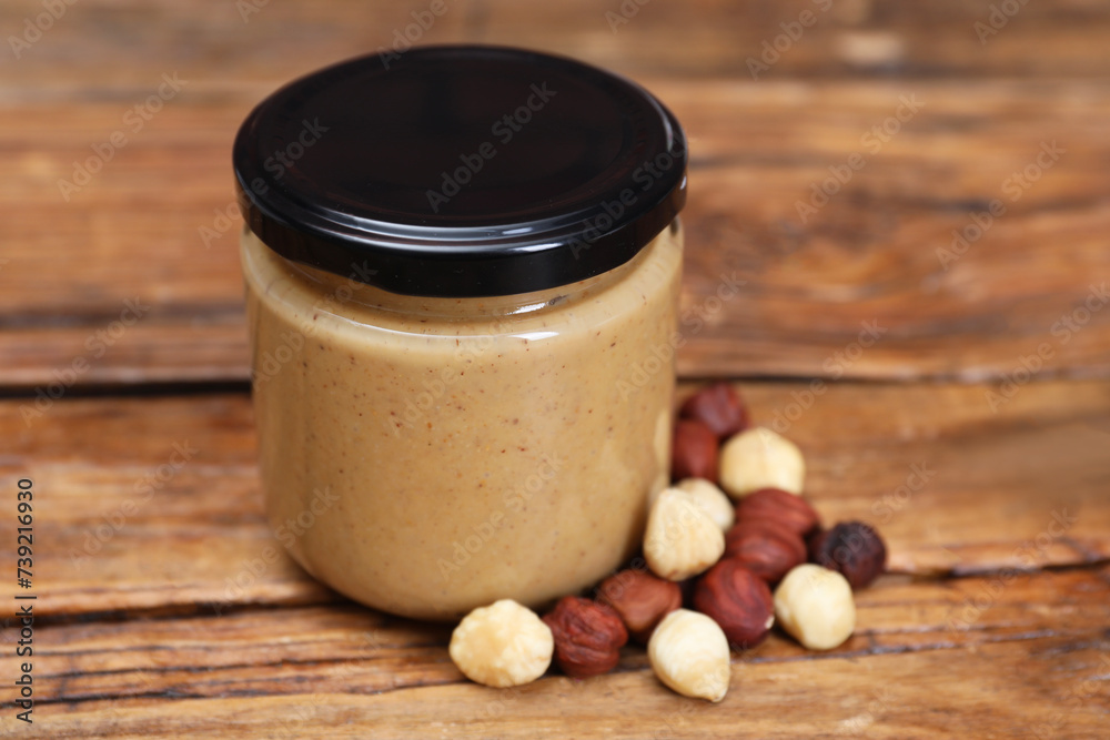 Tasty nut paste in jar and hazelnuts on wooden table, closeup Tasty nut paste in jar and hazelnuts on wooden table, closeup