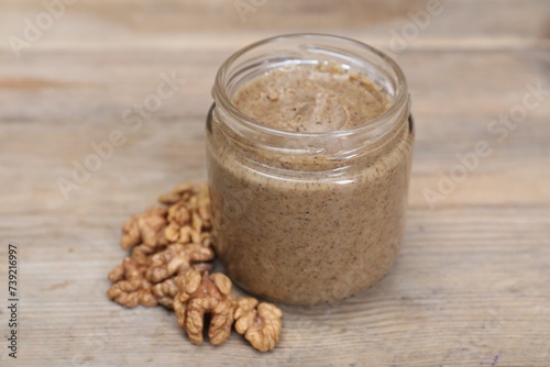 Tasty nut paste in jar and walnuts on wooden table  closeup