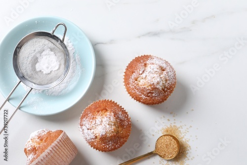 Bilde på lerret Delicious sweet muffins, plate and sieve on white marble table, flat lay, Space
