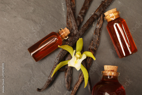 Aromatic vanilla extract, pods and flower on black table, flat lay
