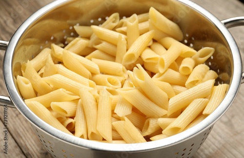 Delicious penne pasta in colander on table, closeup