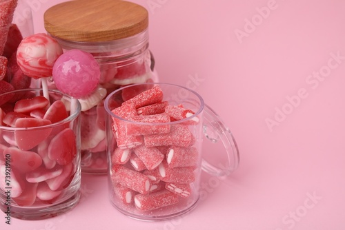 Tasty candies in glass jars on pink background, closeup. Space for text