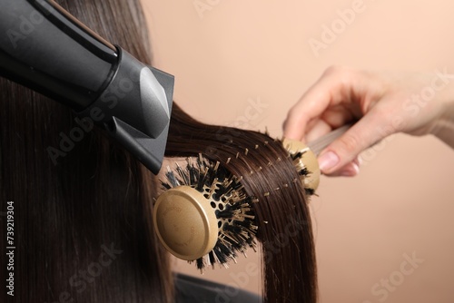 Hairdresser blow drying client's hair on beige background, closeup
