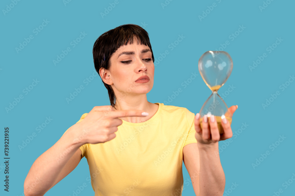 portrait of a serious irritated angry woman holding an hourglass sand timer, aging, deadline process concept