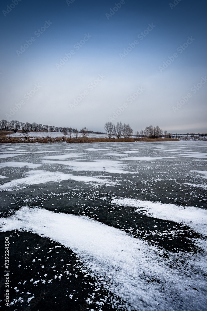 Landscape on the water . Frozen lake . Winter on the lake . Blue clouds and sun . Trees and sun . Winter landscape . Snow on ice . Blizzard in nature 