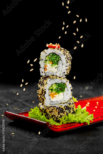 Stack of vegetarian sushi rolls sprinkled by sesame seeds on red plate