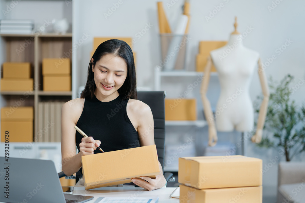 woman start up small business owner writing address on cardboard box at workplace.small business entrepreneur SME or freelance woman working with box at home.