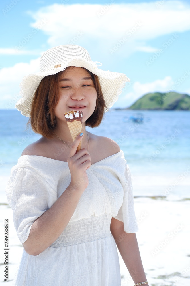 Popsicles,and portraits of women on the beach on vacation, vacation trips and mockups with summer hats. Happiness, ice cream and female tourists eating by the beach and enjoying snacks on Lombok beach Popsicles,and portraits of women on the beach on vacation, vacation trips and mockups with summer hats. Happiness, ice cream and female tourists eating by the beach and enjoying snacks on Lombok beach