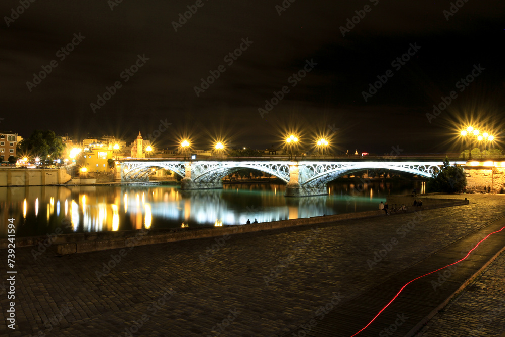 The Puente de Isabel II popularly known as Triana Bridge is a bridge located in Seville (Andalusia Spain) which connects the downtown with the Triana district across the river Guadalquivir.