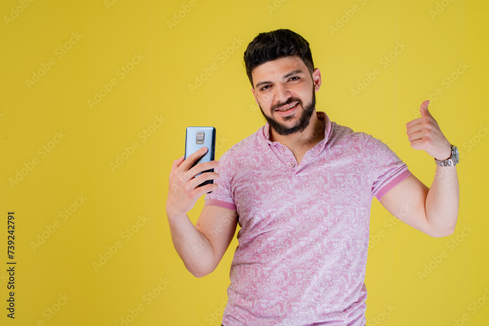 Front view of brunette, handsome male with beard posing indoors, smiling, holding smartphone, taking photo. Concept of youth. Front view of brunette, handsome male with beard posing indoors, smiling, holding smartphone, taking photo. Concept of youth.